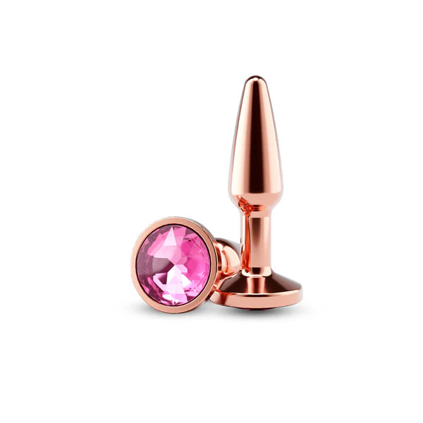 Rose gold tapered plug standing upright next to pink gem on bottom of plug